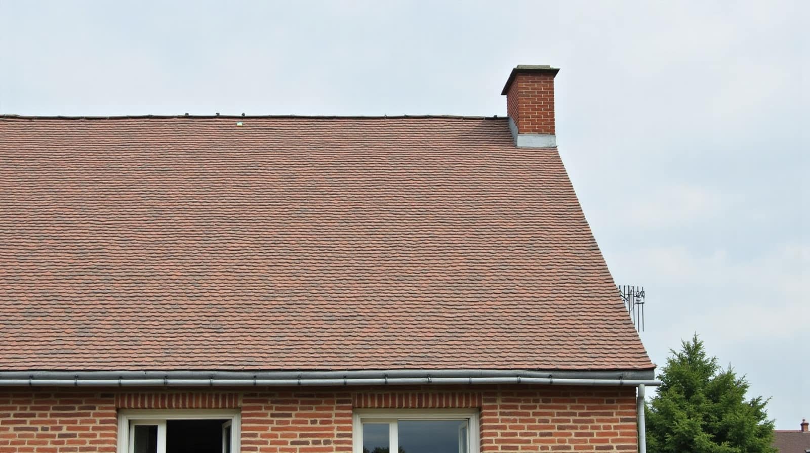 Pan de toiture en tuiles plates avec cheminée en brique et façade en briques en dessous