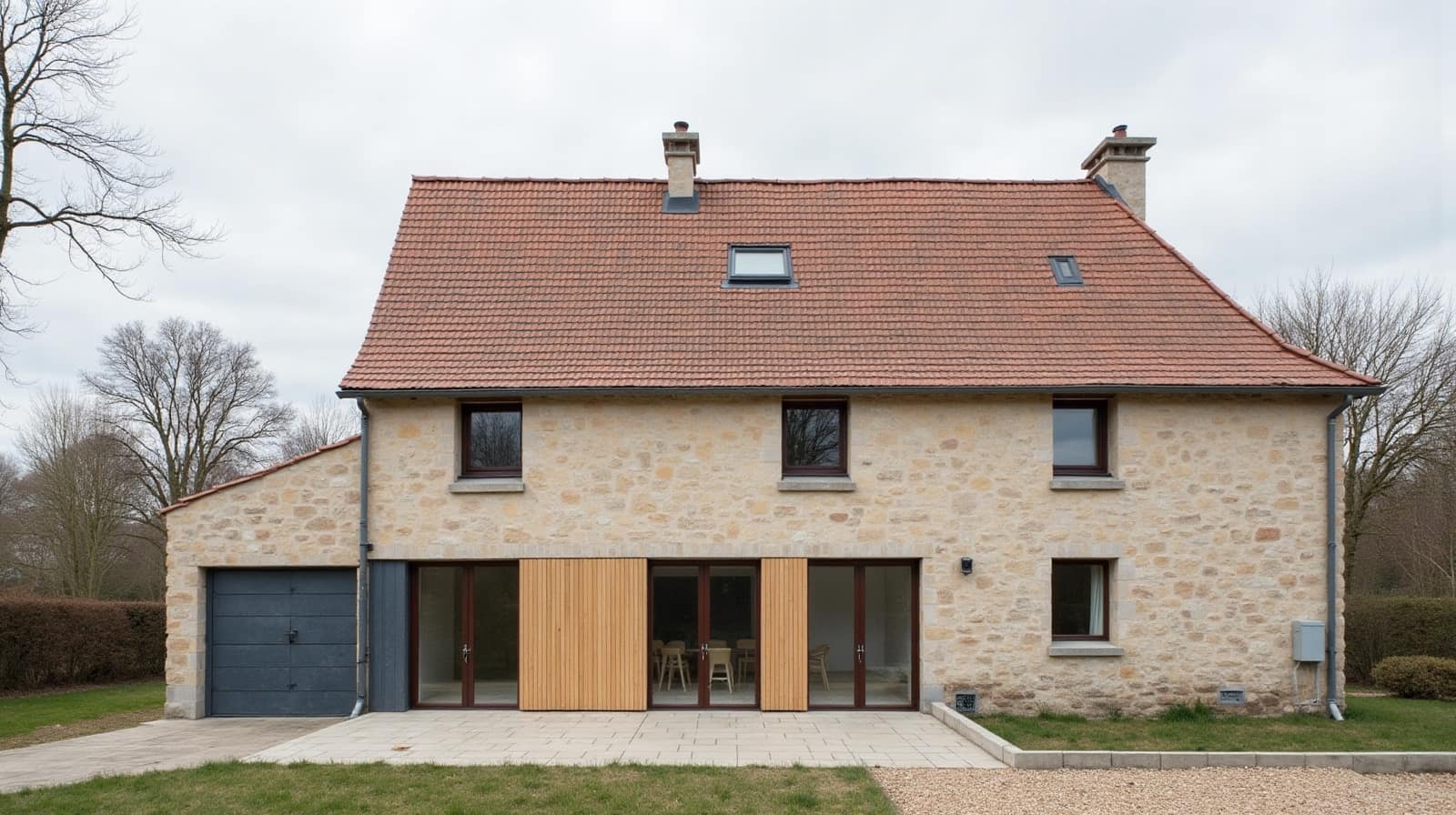 Maison en pierre avec toiture en tuiles orangées, deux fenêtres de toit et garage attenant