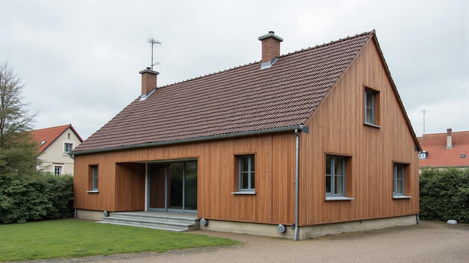 Maison à bardage bois avec toiture en tuiles plates brunes et cheminée en brique